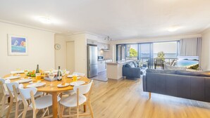 A modern living room with a dining area, a kitchen, and a balcony with a view of the sea. - Florentine, 7 11 Columbia Close - wifi, air conditioned unit with fantastic views of Little Beach (Nelson Bay)