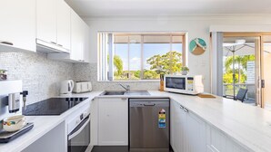 Una cocina moderna con armarios blancos, encimera negra, horno empotrado, lavavajillas y ventana con vistas a zonas verdes.