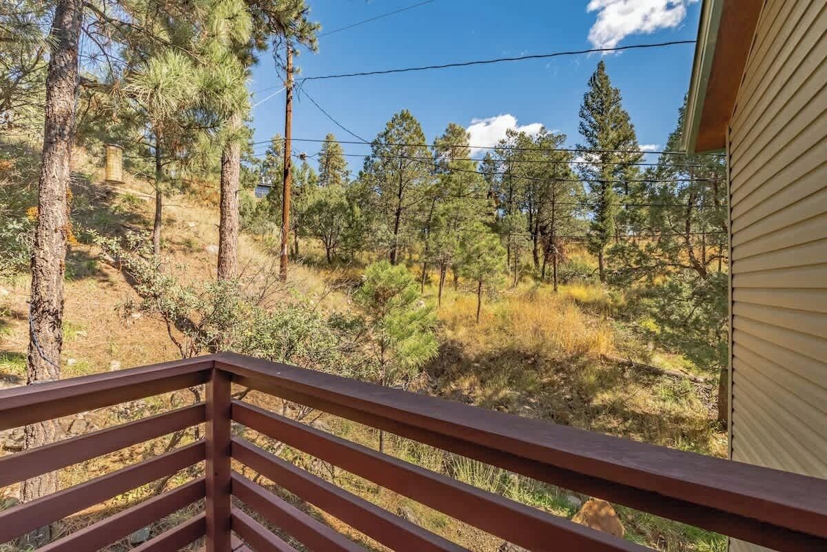 A balcony with a view of a forested area, a wooden railing, and a building with siding.