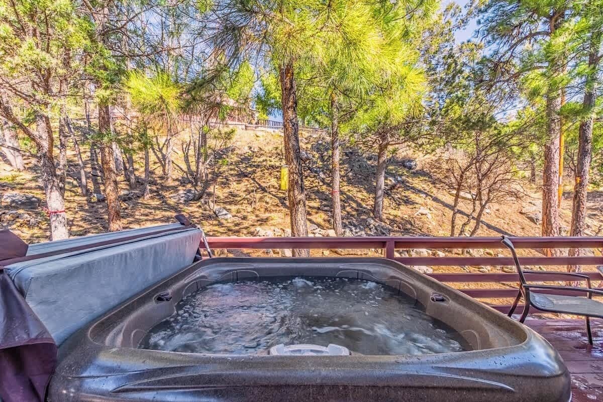 Un bain à remous sur une terrasse en bois, avec vue sur des pins et une colline rocheuse.