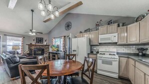 A spacious living room with a fireplace, a dining area with a wooden table and chairs, and a kitchen with wooden cabinets and a stove. - 3 Bears Cottage | Pet Friendly & Hot tub & Pines! (Ruidoso)