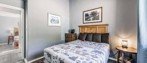 A bedroom with a bed, a wooden headboard, a nightstand, a lamp, and a framed picture on the wall.