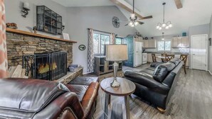 A living room with a fireplace, leather sofas, a dining area, and a kitchen. - 3 Bears Cottage | Pet Friendly & Hot tub & Pines! (Ruidoso)