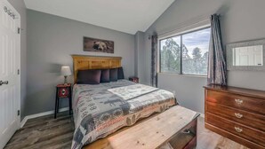 A bedroom with a bed, a wooden headboard, a nightstand, a dresser, a window with a view, and a ceiling fan. - 3 Bears Cottage | Pet Friendly & Hot tub & Pines! (Ruidoso)