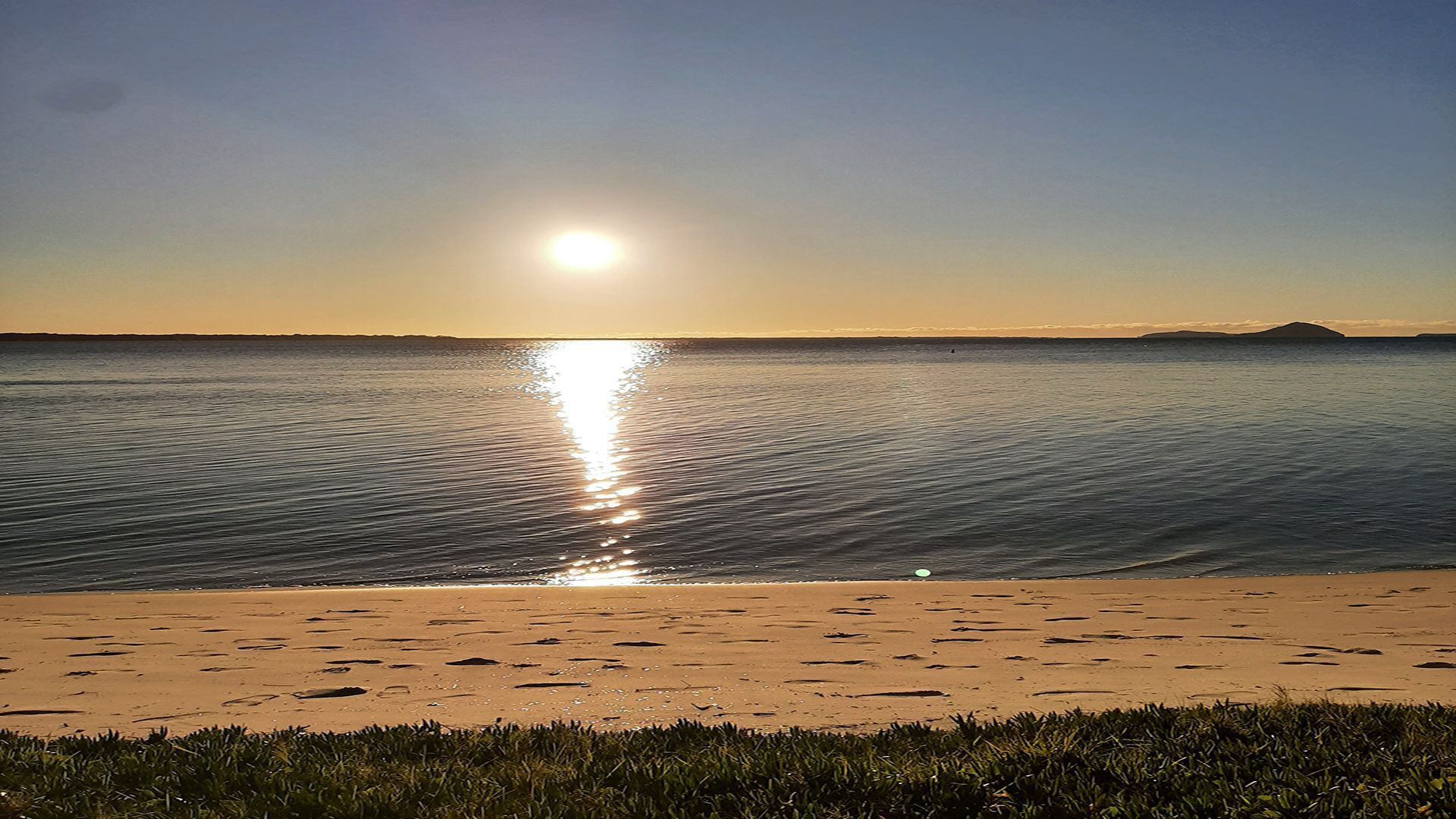A beach with a clear view of the ocean and a distant landmass.