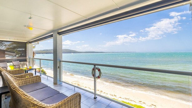 Ein überdachter Außenbereich mit Korbmöbeln und Blick auf Strand und Meer.