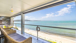 Un espace extérieur aménagé, abrité et doté de mobilier en osier, offrant une vue sur la plage et la mer.