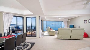 Amplia sala de estar con un ventanal que ofrece vistas al mar, un comedor con mesa y sillas, y un rincón de estar con sofá y sillones.