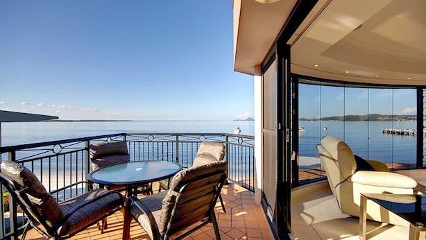 Un balcón con mesa y sillas, vista al mar y una puerta de vidrio que da a un espacio interior.