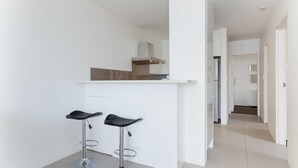 A modern kitchen with white cabinetry and a built-in stove. There are two black bar stools with metal legs. - Collendina, 4/19 Kurrawa Close - fantastic water views and sea breezes (Nelson Bay)
