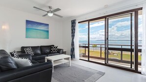 A modern living room with a black leather sofa, a white coffee table, and a painting of a beach. - Collendina, 4/19 Kurrawa Close - fantastic water views and sea breezes (Nelson Bay)