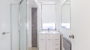 A modern bathroom with a glass shower door, a tiled backsplash, a white sink with a window above, and a mirror. - Fleetwood, 2/63 Shoal Bay Road - spectacular views (Shoal Bay)