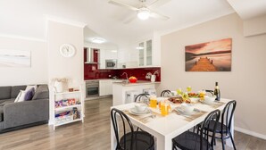 A modern kitchen with white cabinets, a red backsplash, and a dining area with a white table set for a meal. - Bushmans, 9 24 Tomaree Street - Spacious townhouse (Nelson Bay)