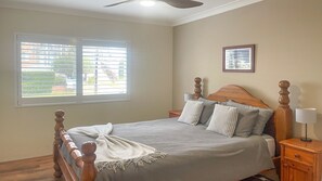 A bedroom with a bed, a nightstand, a lamp, a ceiling fan, and a window with blinds. - Paradiso, 3,4 Laman Street - Comfortable unit with water views, aircon, solar heated pool and in the heart of town (Nelson Bay)