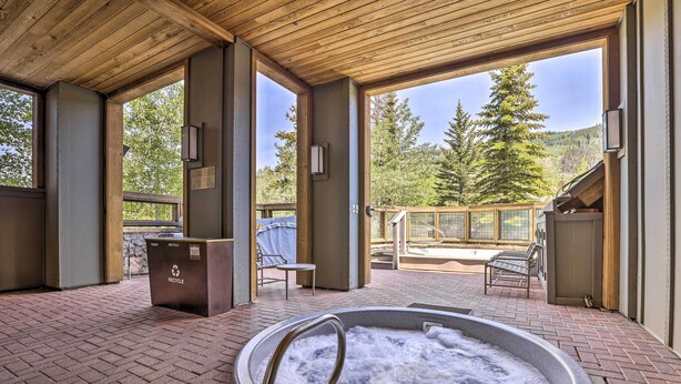 Et område med jacuzzi, træloft, skraldespand og udsigt til træer og bjerge.