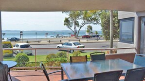 A balcony with a view of the sea, cars parked along the street, and a table with chairs. - Florentine, 4/11 Columbia Close - spectacular views and air conditioning (Nelson Bay)