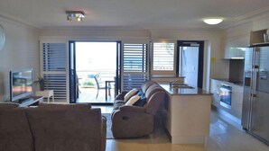 A modern living room with a sofa, a flat-screen TV, and a sliding glass door leading to an outdoor patio. - Florentine, 4/11 Columbia Close - spectacular views and air conditioning (Nelson Bay)