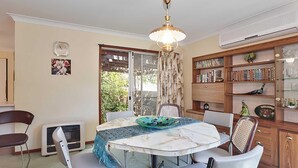A dining area with a round table, chairs, a decorative bowl, a ceiling fan, a bookshelf, and a window with curtains.
