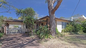 A residential house with a garage, a large tree in front, and a well-maintained lawn.
