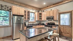 A kitchen with wooden cabinets, a stainless steel refrigerator, a microwave, and a large island with stools.