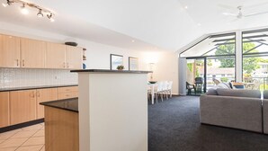 Eine moderne Küche mit Holzsäulen, einer zentralen Kochinsel und einem Essbereich mit grauem Sofa und Stühlen.
