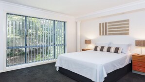 Ein Schlafzimmer mit großem Fenster, einem Bett mit weißer Bettwäsche, zwei Nachttischen mit Lampen und einem Wandbild.