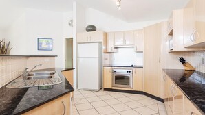 Eine moderne Küche mit hellen Holzschränken, einer Edelstahlspüle, einem weißen Kühlschrank und einem Einbauofen.