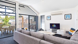 Ein modernes Wohnzimmer mit einem grauen Sofa, einem Flachbildfernseher und einem Essbereich mit Tisch und Stühlen.