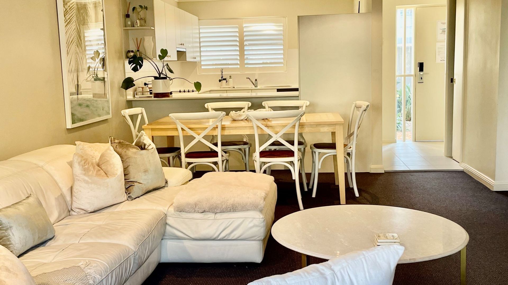 A modern living room with a beige sofa, a round coffee table, and a dining area with white chairs and a wooden table.