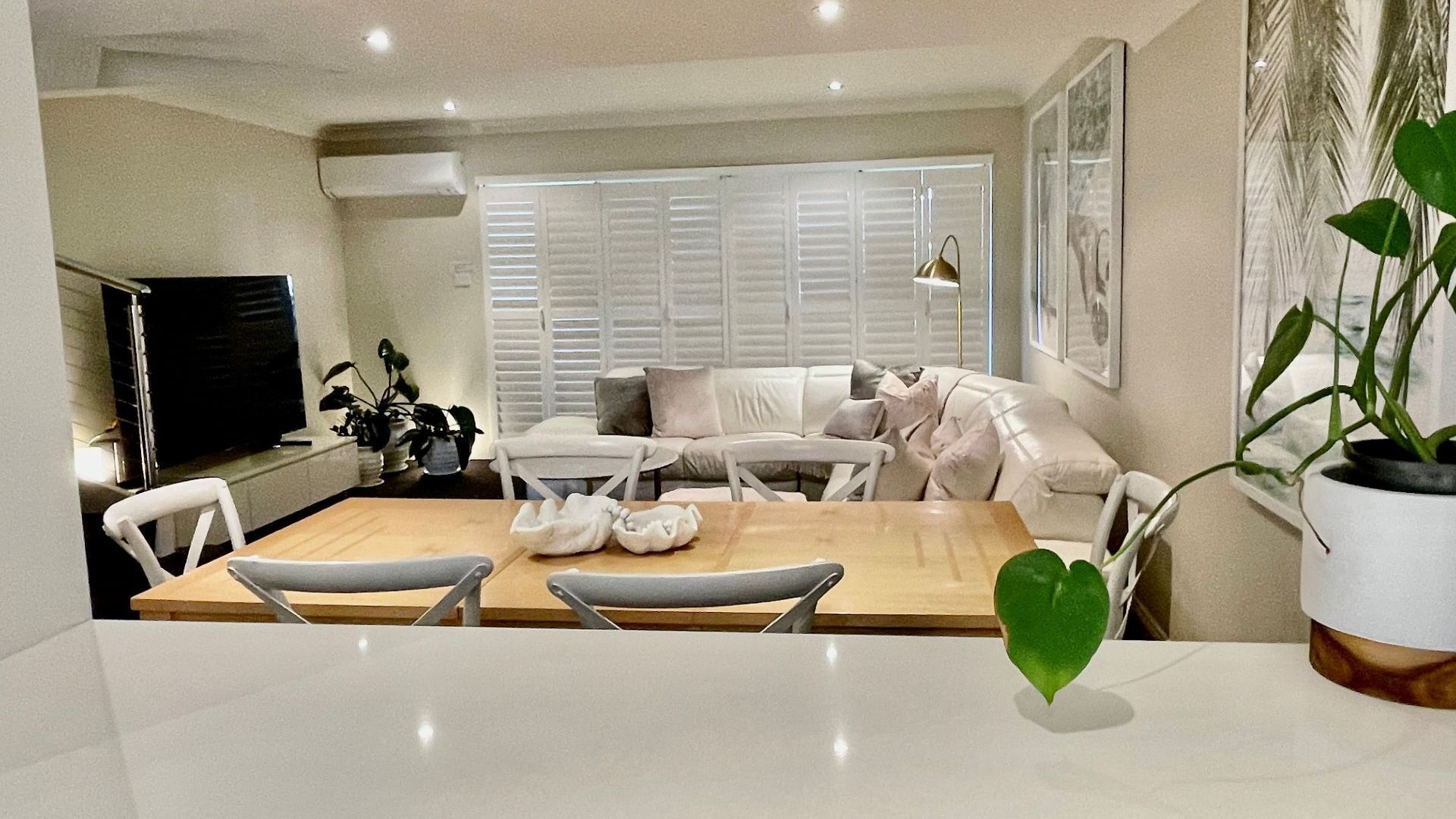 A modern living room with a sofa, chairs, a dining table, and a TV.