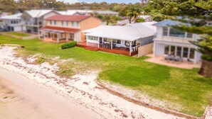 A beachfront property with a covered patio, a lawn, and a sandy beach. - Beached Inn, 93 Foreshore Drive - Spacious beach front house (Salamander Bay)