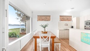 A modern kitchen with white cabinets, a wooden dining table, and a view of the sea. - Beached Inn, 93 Foreshore Drive - Spacious beach front house (Salamander Bay)