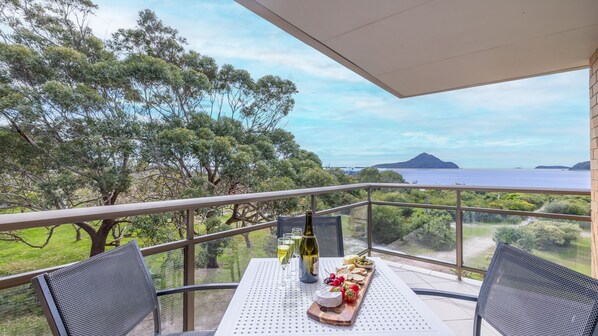 A balcony with a table set for a meal, overlooking a scenic view of the sea and distant land. - Intrepid, 6/3 Intrepid Close - right on the waterfront (Nelson Bay)