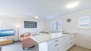 A modern kitchen with a large island, white cabinetry, and a dining area with a table set for two. - Intrepid, 6/3 Intrepid Close - right on the waterfront (Nelson Bay)