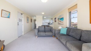 A spacious living area with a grey sofa, a dining table, and a kitchen in the background. - Luskin Lodge, 11/29 Weatherly Close - stunning water views (Nelson Bay)