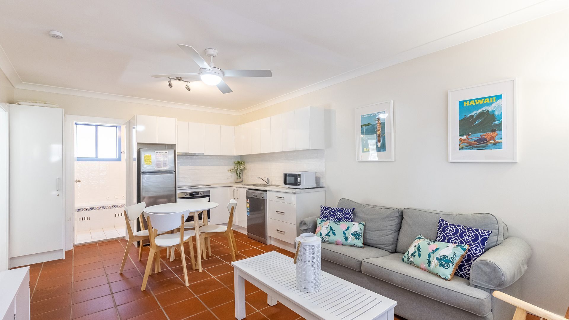 A compact living space with a kitchenette, a dining area with a table and chairs, a sofa with patterned cushions, and a ceiling fan.