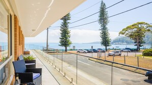 A balcony with a view of the sea, a parking area, and a row of potted plants. - Shoal Towers, unit 1 11 Shoal Bay Road -  fantastic unit across the road from beach with Wi-Fi (Shoal Bay)