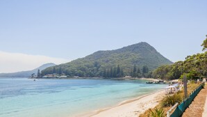 A beach with clear turquoise water, a sandy shore, and a forested hill in the background. - Shoal Towers, unit 1 11 Shoal Bay Road -  fantastic unit across the road from beach with Wi-Fi (Shoal Bay)