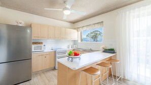 A modern kitchen with light wood cabinets, stainless steel appliances, a white countertop, and a view of the outdoors through a window. - Shoal Towers, unit 1 11 Shoal Bay Road -  fantastic unit across the road from beach with Wi-Fi (Shoal Bay)