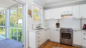Een moderne keuken met witte kasten, een roestvrijstalen oven en een groot raam met uitzicht op groen.