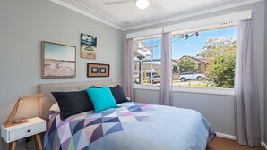 Een slaapkamer met een bed, nachtkastje, plafondventilator en een groot raam met gordijnen.