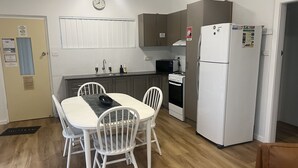 Ett kompakt kök med vita skåp, ett vitt kylskåp, en mikrovågsugn och en spis. Där finns också ett matbord med fyra stolar.