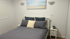 Ett sovrum med en säng, två sängbord, en vägglampa och en tavla som föreställer en strand.