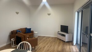 Ett vardagsrum med en brun soffa, ett soffbord, en tv på ett tv-bord och en skjutdörr i glas som leder ut till en balkong.
