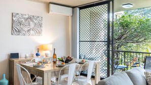 Comedor con mesa de madera, sillas blancas y balcón con vistas a la vegetación.
