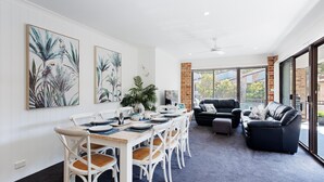 A dining area with a table set for six, surrounded by white chairs with woven seats. - Bay Parklands, 68 2 Gowrie Ave - Fully ducted aircon, wifi, pool, tennis court, communal spa (Nelson Bay)