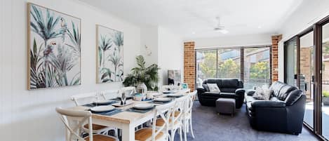 A dining area with a table set for six, surrounded by white chairs with woven seats.