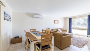 A modern living room with a wooden dining table, two sofas, and a large window with curtains. - Happy Tails , 55 Pantowora Street - pet friendly, air conditioned (Corlette)
