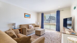 A living room with a sofa, ottoman, and a TV on a wooden table. - Happy Tails , 55 Pantowora Street - pet friendly, air conditioned (Corlette)