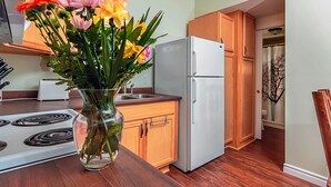 A kitchen with wooden cabinets, a white refrigerator, a stove, and a vase with flowers on the counter. - Newly Renovated, Waterfront Cottages located in Prince Edward County (Milford)
